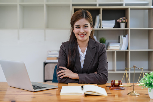 Attractive young lawyer in office Business woman and lawyers with brass scale on wooden desk in office. Law, legal services, advice, Justice and real estate concept.