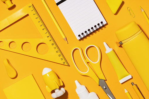 Assorted office and school white and yellow stationery. copy space for back to school or education craft office work concept. Bright Yellow monochrome scissors, rocket notepad. Achievement and success