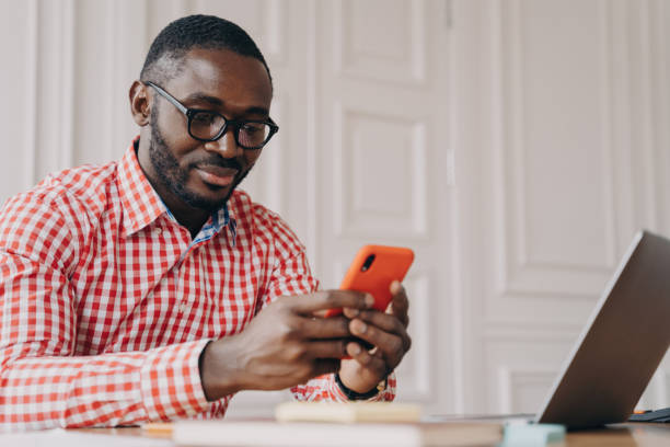 istock Young handsome african male executive in glasses sitting at office table and using mobile phone 1497118636