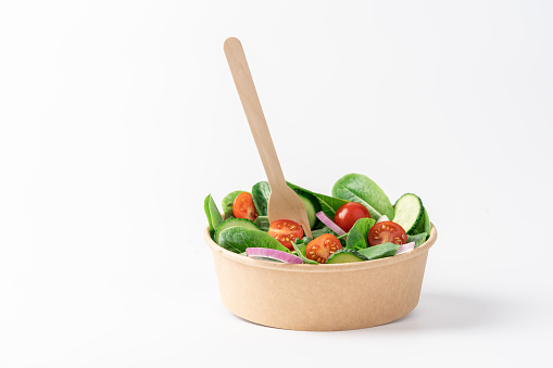 Fresh green salad in cardboard bowl on white background with copy space