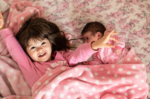 A picture of a toddler and her little sister waking up and lying in bed.