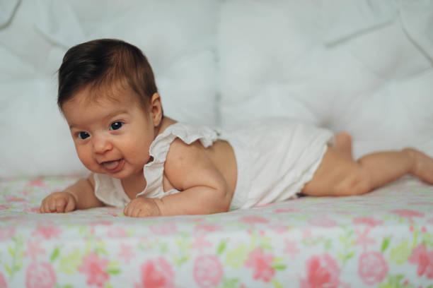 The baby girl is in the crib, on her stomach. She is trying to see everything around her.