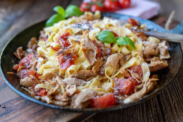 Delicious italian pasta dish with roasted and shredded chicken meat, tomatoes, onions, herbs, garlic and parmesan cheese. Served ready to eat in rustic iron pan on wooden table. Closeup