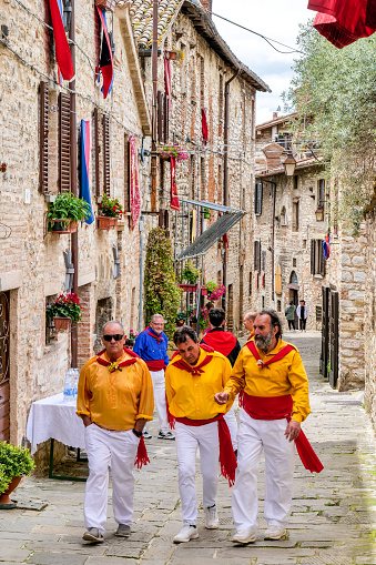 Gubbio, Umbria, Italy, May 15 -- A scene of the traditional and ancient Festa dei Ceri in the historic heart of the medieval town of Gubbio in Umbria. The celebration consists of a race of three wooden columns weighing almost 300 kg each, called Ceri, carried on the shoulders of dozens of bearers, on top of which are placed the statues of Sant'Ubaldo (Saint Ubaldo) protector of Gubbio, San Giorgio (Saint George) and Sant'Antonio Abate (Saint Anthony). The race develops along the streets and alleys of Gubbio up to the summit of Monte Ingino where the Basilica of Sant'Ubaldo is located. This religious celebration, much loved by the whole community of Gubbio, is considered one of the oldest in Italy and in the world and its origins date back to the 12th century. In the photo: Some bearers of the Ceri walk along a medieval stone alley of Gubbio before the start of the race. Image in high definition quality.