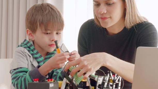 Elementary student remotely learn online at home with parent in make assemble and repair robotics with application on laptop, enjoy creative activity in living room at home. Activities to enhance imagination. Innovation and technology for education. Homeschooling.