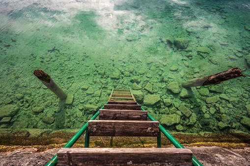 An old wooden poles in green water with a set of stairs leading up to the water in the background