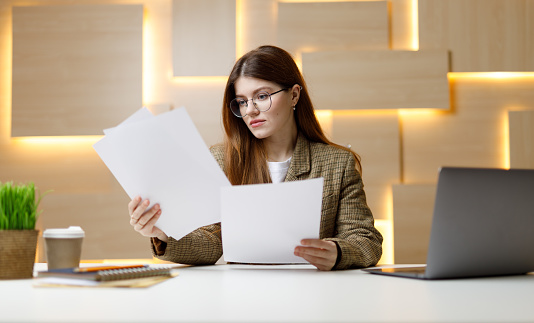 Attractive female businesswoman with papers in her hands at the workplace at the table.