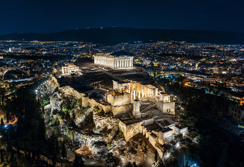 Aerial night view of the illuminated Parthenon Temple at the Acropolis of Athens, Greece, with the city skyline in the background