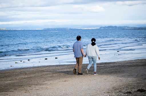 Couple holding hands and walking on beach.  Auckland.