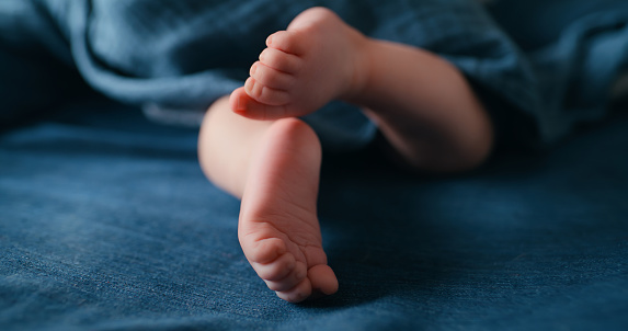 Newborn, feet and sole in bedroom, closeup and sleeping in family home with care, relax and development. Baby, infant kid and zoom of foot for new life in bed, sheets and blanket in nursery at house