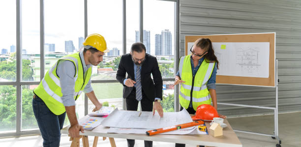 istock Construction engineer and architect in vest and helmet discussing blueprint with construction manager, standing on construction site. 1497135182