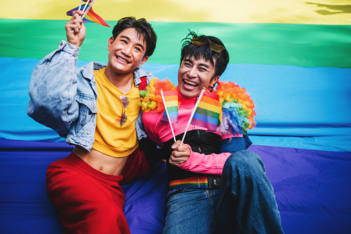 Homosexual couple with two men celebrating LGBT pride together. Holding rainbow flag and cheering