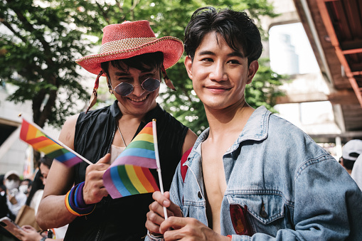 Portrait of a asian man holding a rainbow flag while waiting the LGBTQI parade