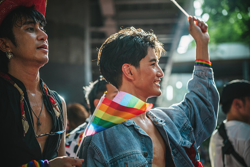Homosexual couple with two men celebrating LGBT pride together. Holding rainbow flag and cheering