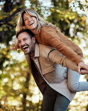 Playful couple having fun while piggybacking with their arms outstretched during autumn day in nature. Copy space.