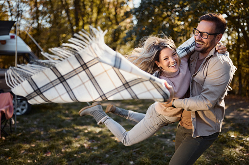 Cheerful couple having fun while spinning during autumn day at trailer park.