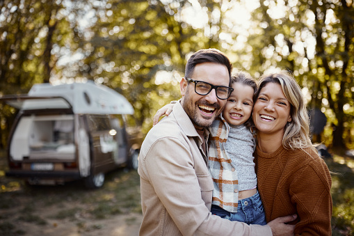 Happy parents and their small daughter embracing while spending an autumn day at trailer park.
