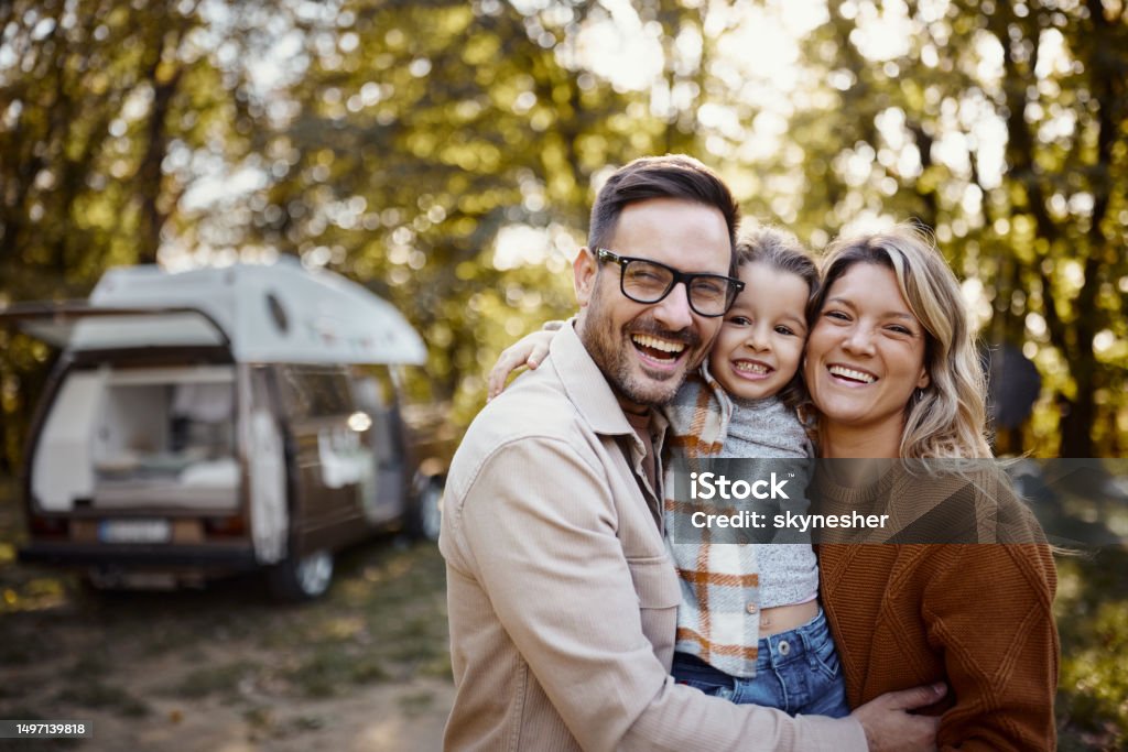 Portrait of happy family in autumn day at trailer park. Happy parents and their small daughter embracing while spending an autumn day at trailer park. Family Stock Photo