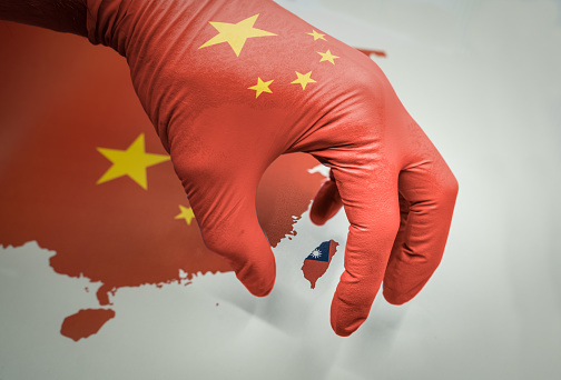 Hand with a glove in the colors of the flag of China grabbing the island of Taiwan. China and Taiwan relations and rising dispute