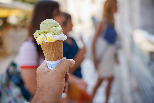 Holding a biscuit cone with ice cream scoops, confectioner's display fridge for orders in the street