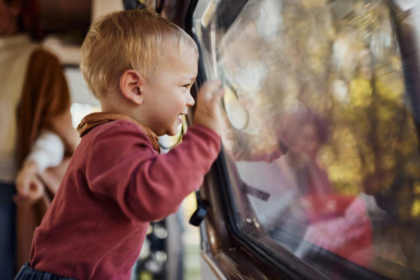 Happy baby boy having fun while looking through a window of camper trailer.