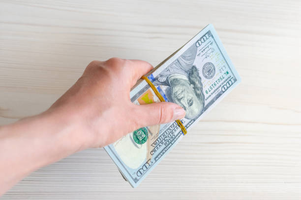 istock A stack of one hundred dollar bills is held by a woman's hand. 1497142618
