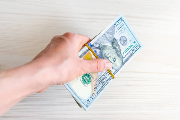 istock A stack of one hundred dollar bills is held by a woman's hand. 1497142632