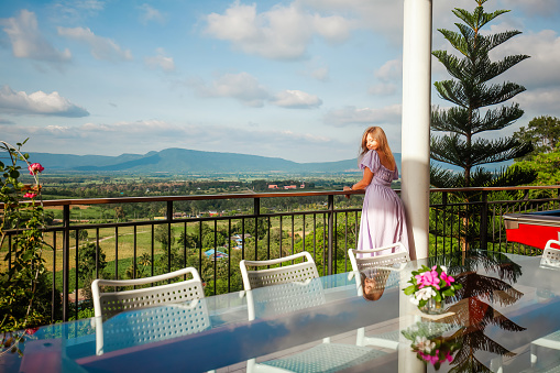 Woman on vacation enjoys beautiful mountain view from a balcony. Summer landscape and blue sky, scenic backdrop, relaxation and travel.