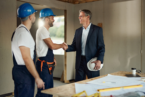 Happy real estate developer shaking hands with one worker at construction site. Copy space.