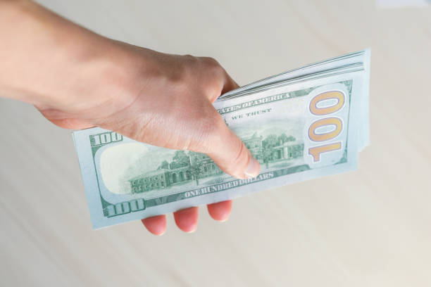 istock A stack of one hundred dollar bills is held by a woman's hand. 1497144191