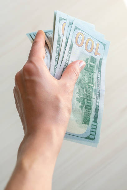 istock A stack of one hundred dollar bills is held by a woman's hand. 1497144245