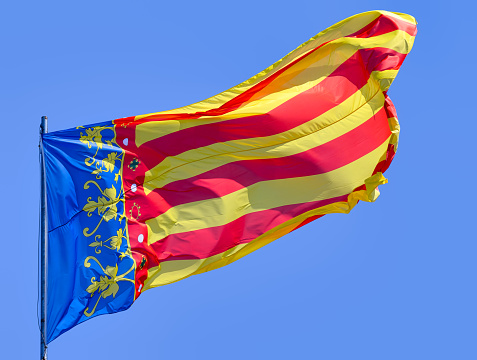 A double exposure shot of a large sunlit Catalan flag against a blue sky