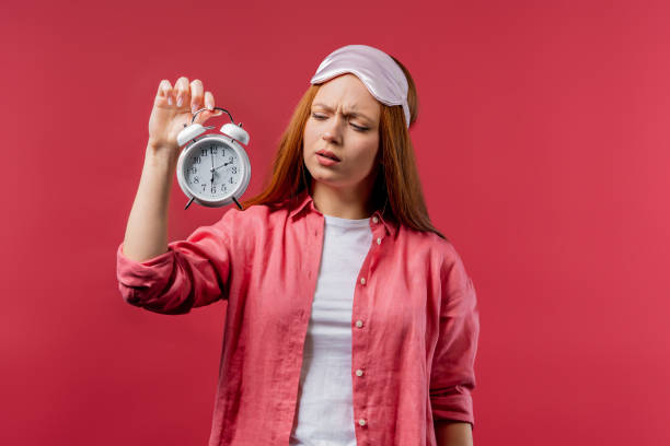 réveillé par une femme endormie du réveil le tenant à la main. fond rose. tôt 6 heures du matin. lazy lady n’a pas assez dormi, concept de temps qui passe. - clock time clock hand urgency photos et images de collection