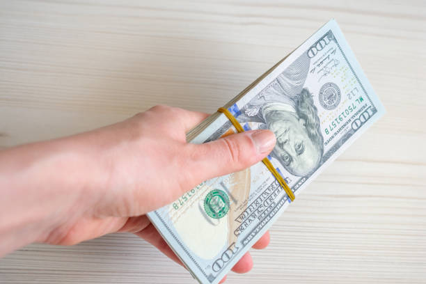 istock A stack of one hundred dollar bills is held by a woman's hand. 1497144688
