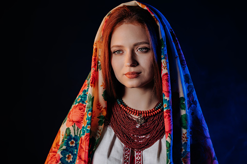 Charming ginger woman in traditional ukrainian handkerchief, necklace and embroidered blouse at black background. Ukraine, style, folk, ethnic culture. High quality photo