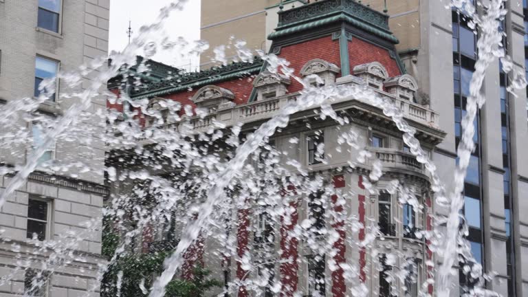 Wild splashing torrents of fountain spray in front of an ornate luxury early century white stone and red orange brick building adorned with copper finishings of teal blue green tarnish