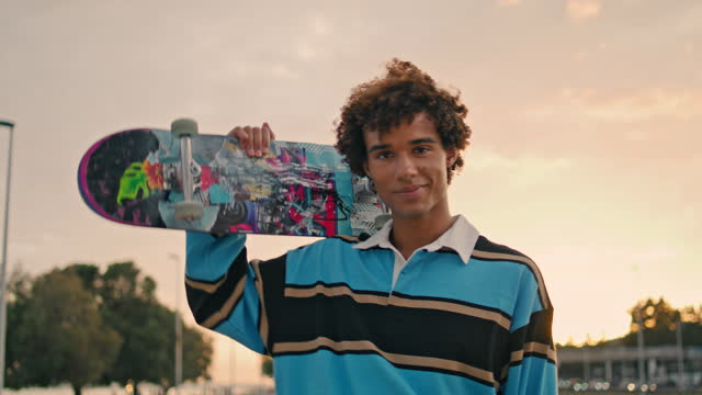 Stylish student holding skate evening city portrait. Smiling man looking camera