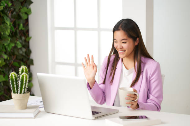 a young asian woman smiling talking on a video call in the coworking room having coffee stock photo
