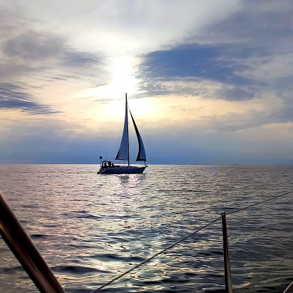 A sailboat heading into harbor in a golden sunset above the water, Lake Michigan, USA.