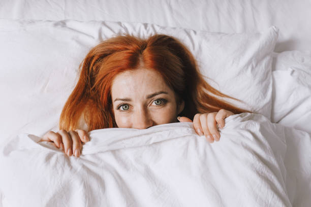 istock coy young woman hiding under bed cover 1497158887