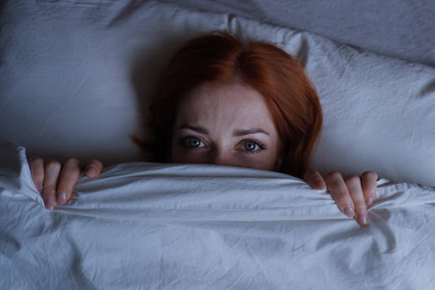 istock sleepless woman lying in bed hiding under duvet at night 1497158961