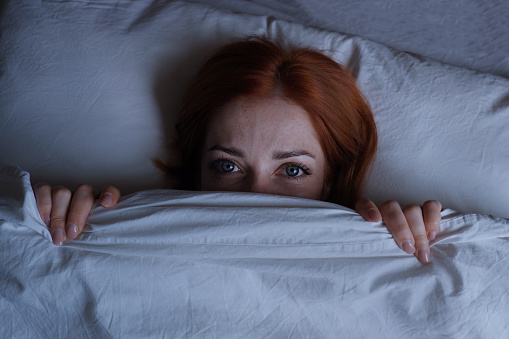 sleepless woman lying in bed with open eyes hiding under duvet at night
