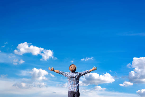 istock Young man's rising hands in a copy space against an abstract blue sky and white cloud background. Concept of adventure travel and freedom. 1497161551