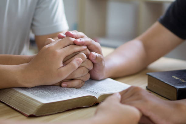 istock Prayer meeting concept.Colleagues shaking hands reading scriptures and praying to God at work place.Prayer, trust, hope, gratitude concept 1497168139