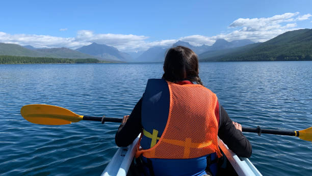 woman sitting in her kayak on lake macdonald in glacier national park admiring the scenery - mcdonald lake imagens e fotografias de stock