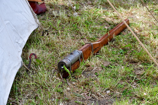 A close up on a wooden bombard or handgun made out of wood and decorated with some metal elements laying next to a cloth tent stretched out with ropes seen on a sunny summer day in Poland