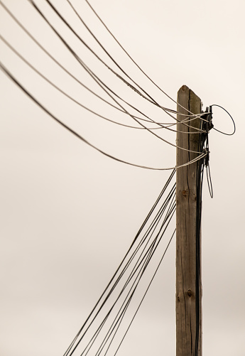 An old telephone pole with cables on natural sky background, vertical