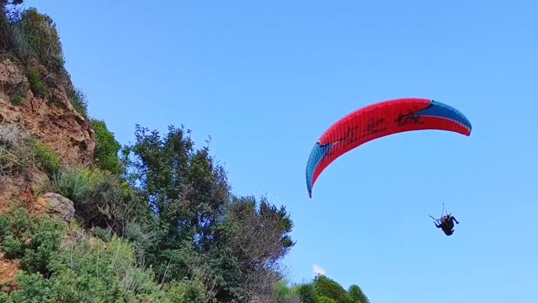 A red paraglider with  pilot flies in the blue sky