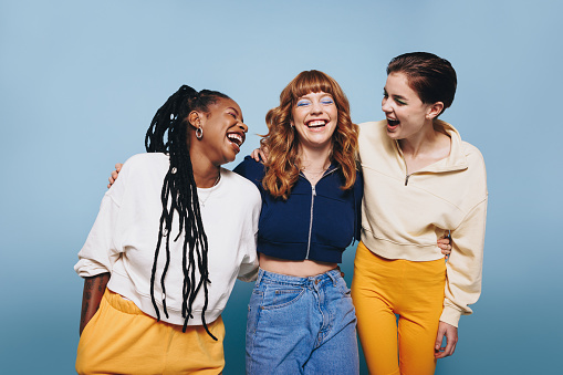 Happy young women laughing together in a studio. Group of female friends having fun while standing together.