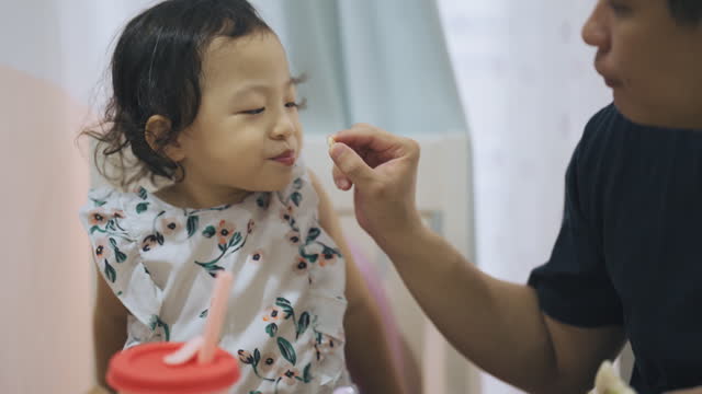 Asian Chinese father feeding baby girl in dining room